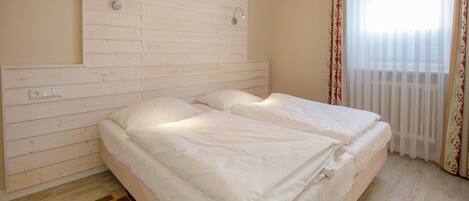 A bedroom with a wooden headboard, a bed with white bedding, a hanging light fixture, and a window with sheer curtains.
