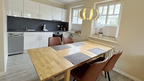 Een moderne keuken met witte kasten, een houten eettafel met placematen en een hanglamp.
