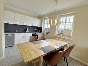 A modern kitchen with white cabinets, a wooden dining table with placemats, and a pendant light.