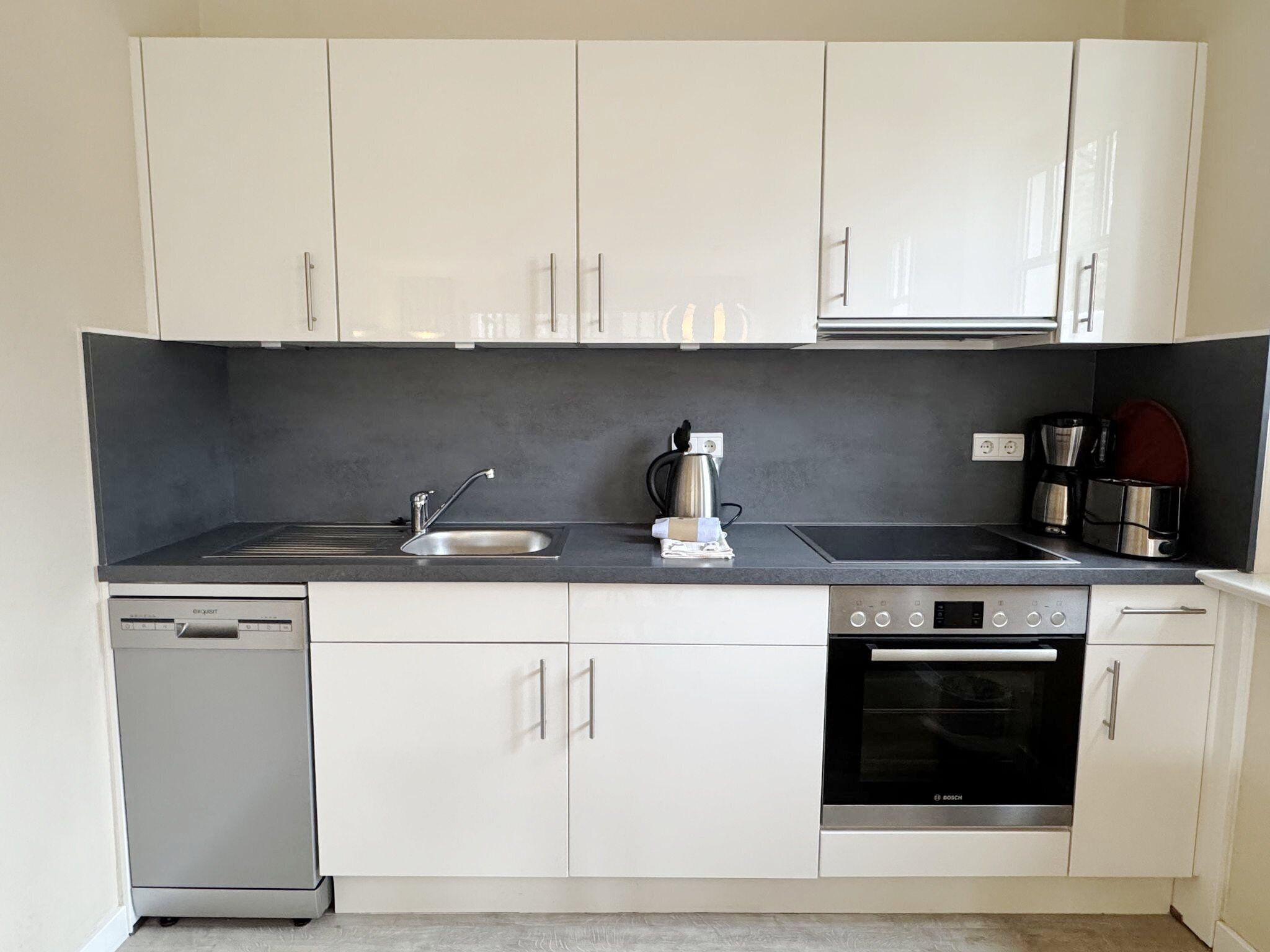 A modern kitchen with white cabinets, a dishwasher, a stove, and a coffee maker.