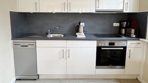 Een moderne keuken met witte kasten, een vaatwasser, een fornuis en een koffiezetapparaat.