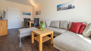 Een moderne woonkamer met een bank, een houten salontafel en een eethoek met stoelen en een tafel.