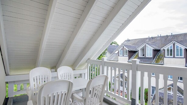 A covered porch with white chairs and a table, overlooking a row of houses. - Comfort apartment with 2 bedrooms and balcony on the top floor (Ostseebad Binz)
