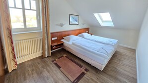 A bedroom with a large window, a skylight, a bed, a nightstand, and a radiator. - Comfort apartment with 2 bedrooms and balcony on the top floor (Ostseebad Binz)