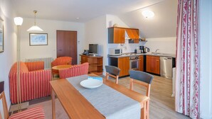 A compact living space with a dining area, a kitchenette, and a seating area with striped sofas. - Comfort apartment with 2 bedrooms and balcony on the top floor (Ostseebad Binz)