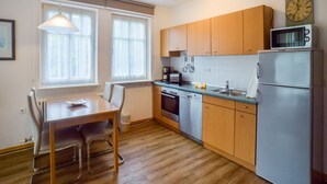 A compact kitchen with wooden cabinets, a stainless steel refrigerator, a microwave, and a dining table with chairs. - Komfort Ferienwohnung mit 1 Schlafzimmer und Terrasse im Erdgeschoss (Ostseebad Binz)
