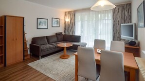 A modern living room with a sofa, dining table, chairs, a TV, and a wooden cabinet. - Komfort Ferienwohnung mit 1 Schlafzimmer und Terrasse im Erdgeschoss (Ostseebad Binz)