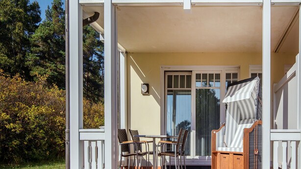 A covered outdoor seating area with a table and chairs, a cushioned bench, and a door leading to a shaded interior space. - Komfort Ferienwohnung mit 1 Schlafzimmer und Terrasse im Erdgeschoss (Ostseebad Binz)