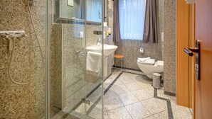 A modern bathroom with a glass-enclosed shower, a sink, a toilet, and a small stool. - Komfort Ferienwohnung mit 1 Schlafzimmer und Terrasse im Erdgeschoss (Ostseebad Binz)