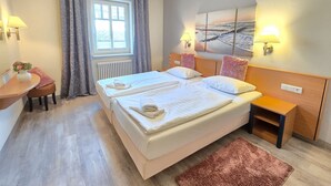 Ett hotellrum med en dubbelsäng, sängbord, ett skrivbord med en stol, ett fönster med gardiner och väggmonterade lampor.