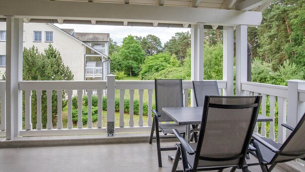 A covered outdoor seating area with a white railing, a table, and four chairs. - Comfort apartment with 1 bedroom and balcony on the upper floor (Ostseebad Binz)