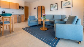 A compact living space with a kitchenette, a sofa set, a dining table, and a small rug. - Comfort apartment with 1 bedroom and balcony on the upper floor (Ostseebad Binz)