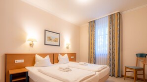 A hotel room with a double bed, two bedside tables, a chair, a desk, and a window with curtains. - Comfort apartment with 1 bedroom and balcony on the upper floor (Ostseebad Binz)