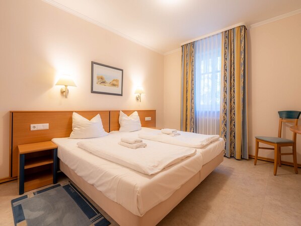 A hotel room with a double bed, two bedside tables, a chair, a desk, and a window with curtains.