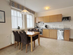 A modern kitchen with wooden cabinets, a built-in microwave, and a dining area with a table and chairs.