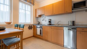 A modern kitchen with wooden cabinets, stainless steel appliances, and a dining area with a table and chairs. - Comfort apartment with 1 bedroom and balcony on the upper floor (Ostseebad Binz)