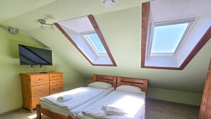 Une chambre avec un lit en bois, une commode en bois et un téléviseur à écran plat. Il y a des fenêtres de toit au plafond.
