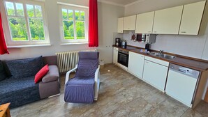 Un espace de vie compact comprenant un canapé, un fauteuil inclinable, un radiateur, une cuisine avec des meubles blancs, un four à micro-ondes et un lave-vaisselle.