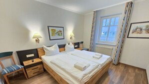 Un letto matrimoniale con lenzuola bianche, due comodini con lampade, una sedia con cuscino a righe e due quadri appesi alle pareti.