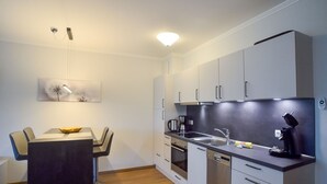 Una cucina moderna con zona pranzo, dotata di elettrodomestici in acciaio inossidabile, lavastoviglie e macchina da caffè.