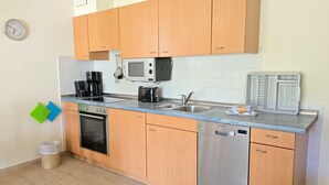 A compact kitchen with wooden cabinets, a microwave, a toaster, a coffee maker, and a dishwasher. - Comfort apartment with 1 bedroom and terrace on the first floor (Ostseebad Binz)