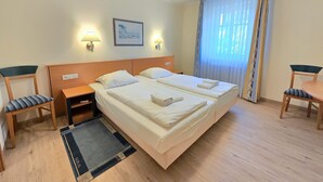 A hotel room with a double bed, two bedside tables, a chair, a desk, a window with curtains, and a framed picture on the wall. - Comfort apartment with 1 bedroom and terrace on the first floor (Ostseebad Binz)