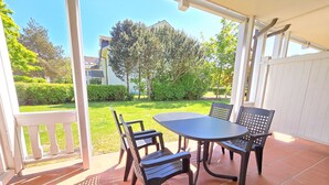 An outdoor patio with a round table and four chairs, surrounded by a white fence and a view of a green garden and buildings in the background. - Comfort apartment with 1 bedroom and terrace on the first floor (Ostseebad Binz)