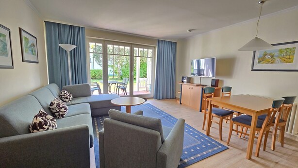 A modern living room with a sofa, a dining table, and a TV. - Comfort apartment with 1 bedroom and terrace on the first floor (Ostseebad Binz)
