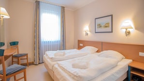 Hotellihuone, jossa on parivuode, työpöytä tuolilla, lamppu ja taulu seinällä.