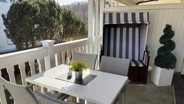 Een terras met een witte tafel en rieten stoelen, een gestreepte luifel en een bloempot.