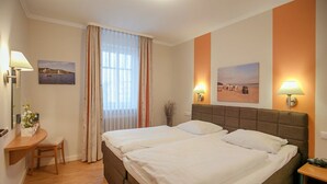 Een hotelkamer met een groot bed, twee bedlampen, een bureau met een stoel, en twee ingelijste foto's aan de muur.