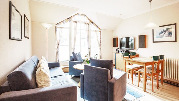 A modern living room with a sofa, armchairs, a coffee table, and a dining area with a table and chairs. - Comfort apartment with 1 bedroom, balcony and bedroom on the top floor (Ostseebad Binz)