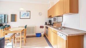 A modern kitchen with wooden cabinets, a microwave, and a sink. There is a dining area with a table and chairs, and a radiator on the wall. - Comfort apartment with 1 bedroom, balcony and bedroom on the top floor (Ostseebad Binz)