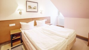 A hotel room with a double bed, two bedside tables, a nightstand, a framed picture on the wall, and a radiator. - Comfort apartment with 1 bedroom, balcony and bedroom on the top floor (Ostseebad Binz)