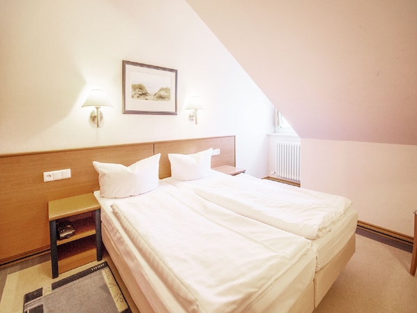Habitación de hotel con cama doble, dos mesitas de noche, un radiador y un cuadro en la pared.