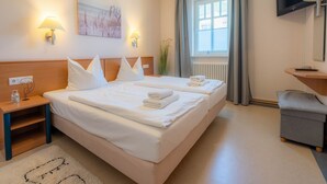 A hotel room with two beds, a TV, a desk, and a window with curtains. - Comfort apartment with 1 bedroom and balcony on the upper floor (Ostseebad Binz)