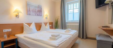 Une chambre d’hôtel avec deux lits, une télévision, un bureau et une fenêtre avec des rideaux.