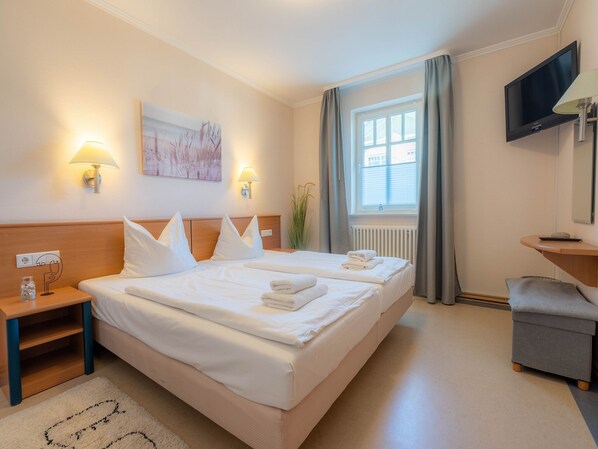 Camera d'albergo con due letti, televisione, scrivania e finestra con tende.