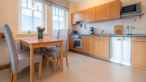 A modern kitchen with wooden cabinets, a built-in oven, microwave, and dishwasher. There is a dining table with chairs and a window with blinds. - Comfort apartment with 1 bedroom and balcony on the upper floor (Ostseebad Binz)