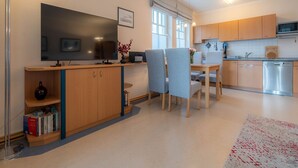 A modern kitchen with wooden cabinets, a built-in oven, and a dishwasher. There is a dining area with a table and chairs, and a flat-screen TV mounted on the wall. - Comfort apartment with 1 bedroom and balcony on the upper floor (Ostseebad Binz)