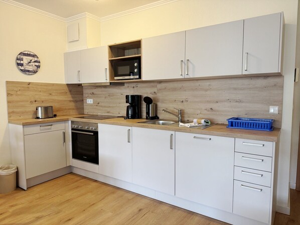 A compact kitchen with white cabinets, a Bosch oven, a microwave, and a wooden countertop.