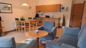 A modern living room with a sofa set, a dining table with chairs, and a kitchen area with wooden cabinets and appliances. - Komfort Ferienwohnung mit 1 Schlafzimmer und Balkon im Obergeschoss (Ostseebad Binz)