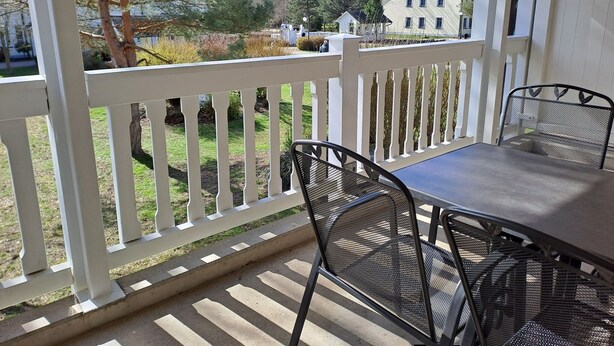 A covered patio with a table and chairs, a white railing, and a view of a house and trees. - Komfort Ferienwohnung mit 1 Schlafzimmer und Balkon im Obergeschoss (Ostseebad Binz)