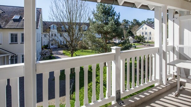 Un balcón con barandilla blanca, con vistas a una zona residencial con casas y césped.