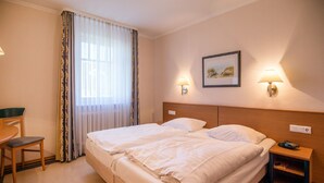 Habitación de hotel con cama doble, escritorio y una silla. Hay dos lámparas de pared y un cuadro en la pared.