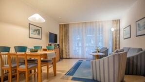 Una sala de estar moderna con comedor, un sofá, un televisor y una ventana con cortinas.