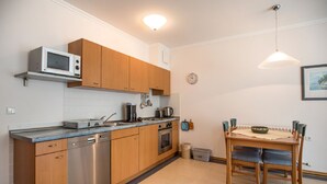 Una cocina compacta con armarios de madera, microondas, lavavajillas y una mesa de comedor con sillas.
