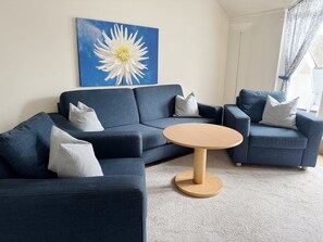 A living room with a sectional sofa, a round coffee table, and a large floral painting on the wall. - Komfortplus Vacation Apartment with 1 bedroom and a balcony on the top floor (Ostseebad Binz)
