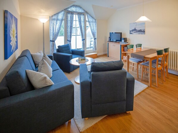 Ein modernes Wohnzimmer mit einer Couch, Sesseln, einem Couchtisch und einem Essbereich mit Tisch und Stühlen.