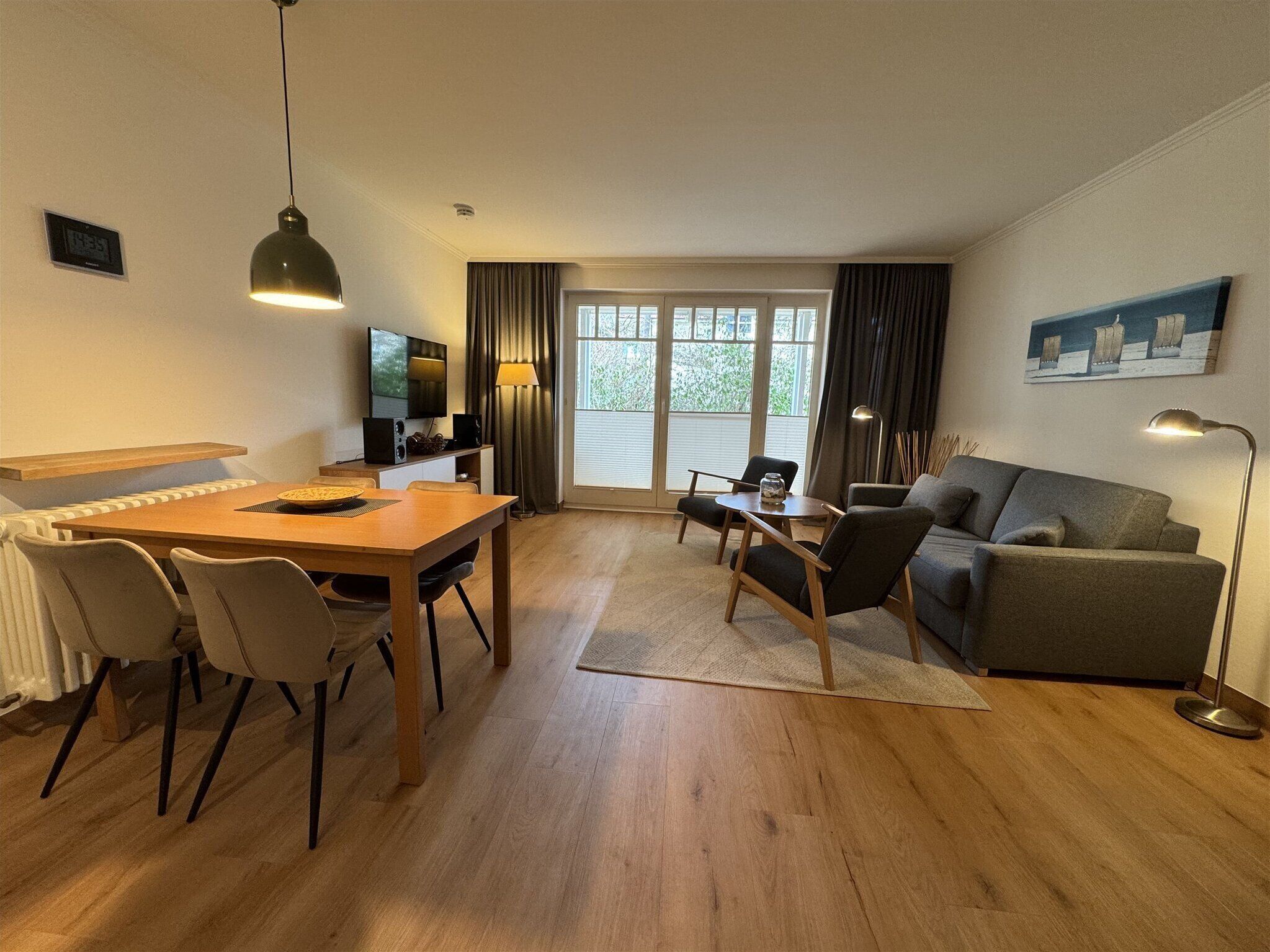 A modern living room with a dining area, a sofa, a TV, and a large window with curtains.